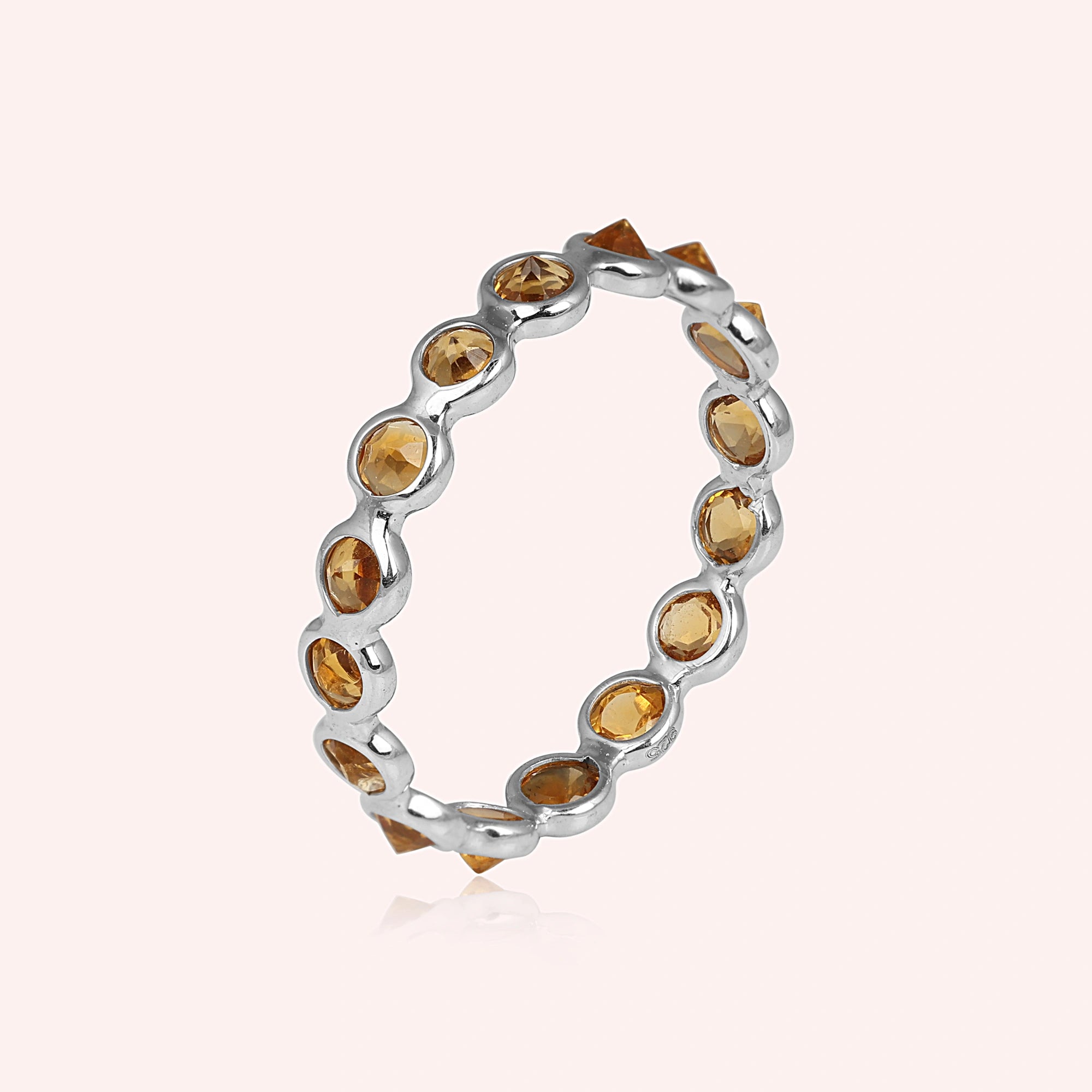 Angled close up shot of a sterling silver citrine ring on a light pink background with round cut yellow citrine stones