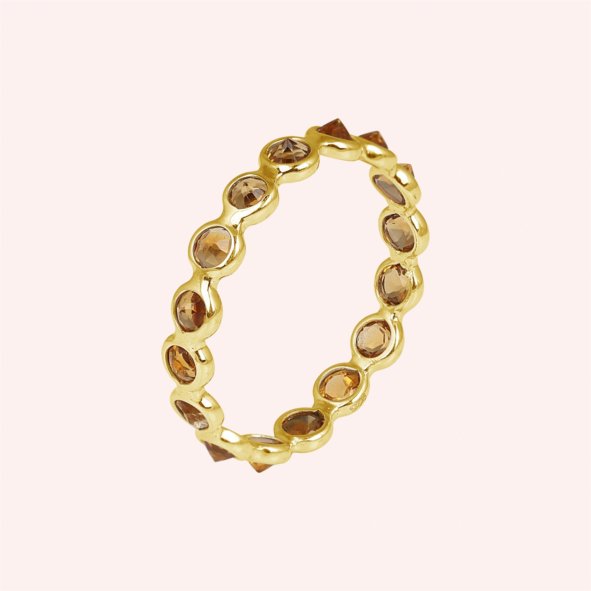 Angled shot of a gold-plated sterling silver citrine ring on a light pink background with round cut yellow citrine stones