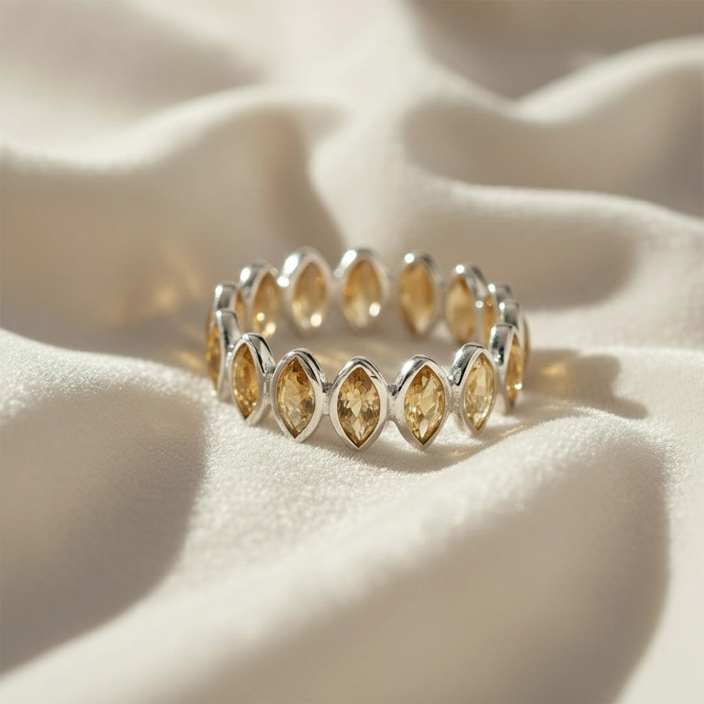 Sterling silver eternity ring with marquise citrine stones on a wrinkled off-white velvet background straight angle view.