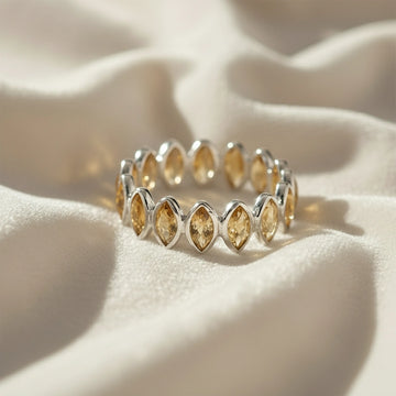 Sterling silver eternity ring with marquise citrine stones on a wrinkled off-white velvet background straight angle view.