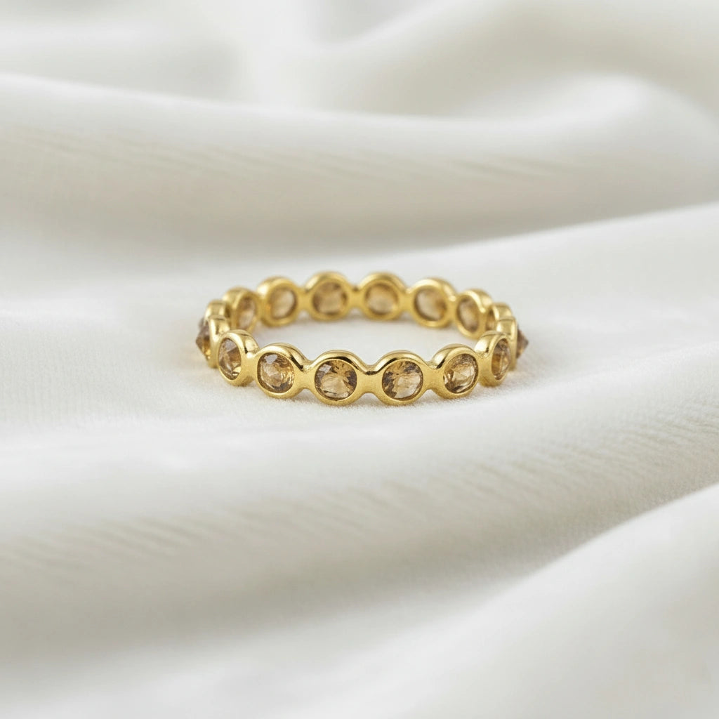 Horizontal close up shot of a gold-plated sterling silver citrine ring on a white velvet background with round cut stones