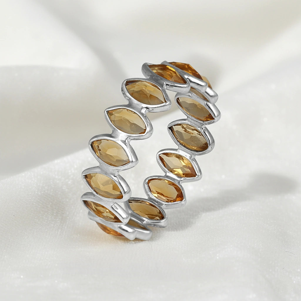 Sterling silver eternity ring featuring marquise citrine stones on a wrinkled white velvet background viewed at an angle.