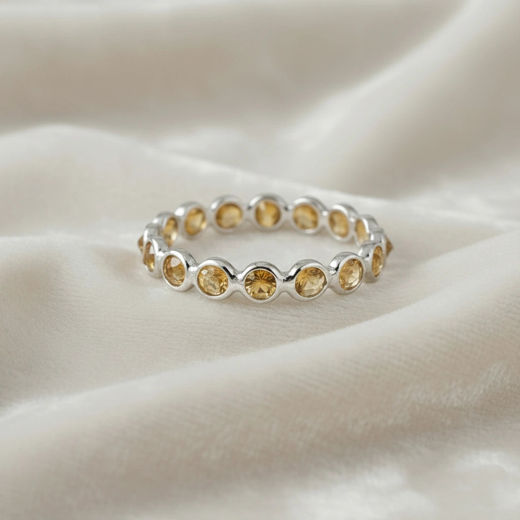 Horizontal shot of a sterling silver citrine ring on a messy off-white velvet cloth with round cut yellow citrine stones