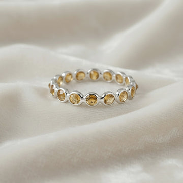 Horizontal shot of a sterling silver citrine ring on a messy off-white velvet cloth with round cut yellow citrine stones