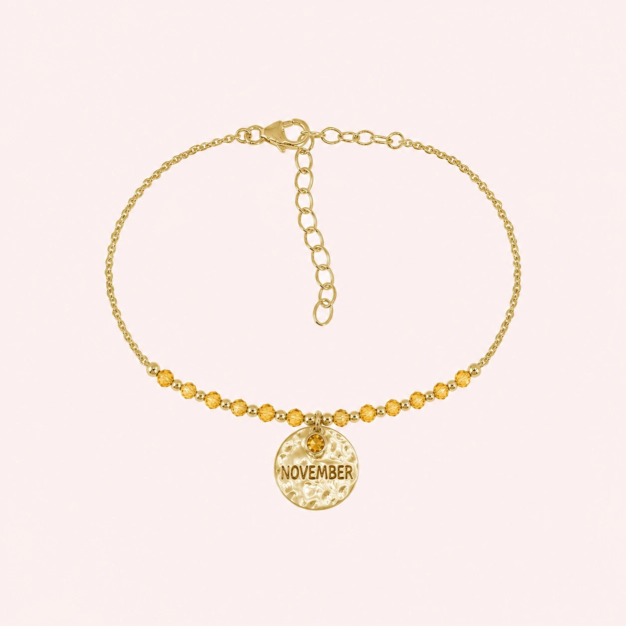 Birthstone_bracelet_in_gold_plated_silver_with_November_charm_and_citrine_beads_on_fine_chain_on_solid_pink_background