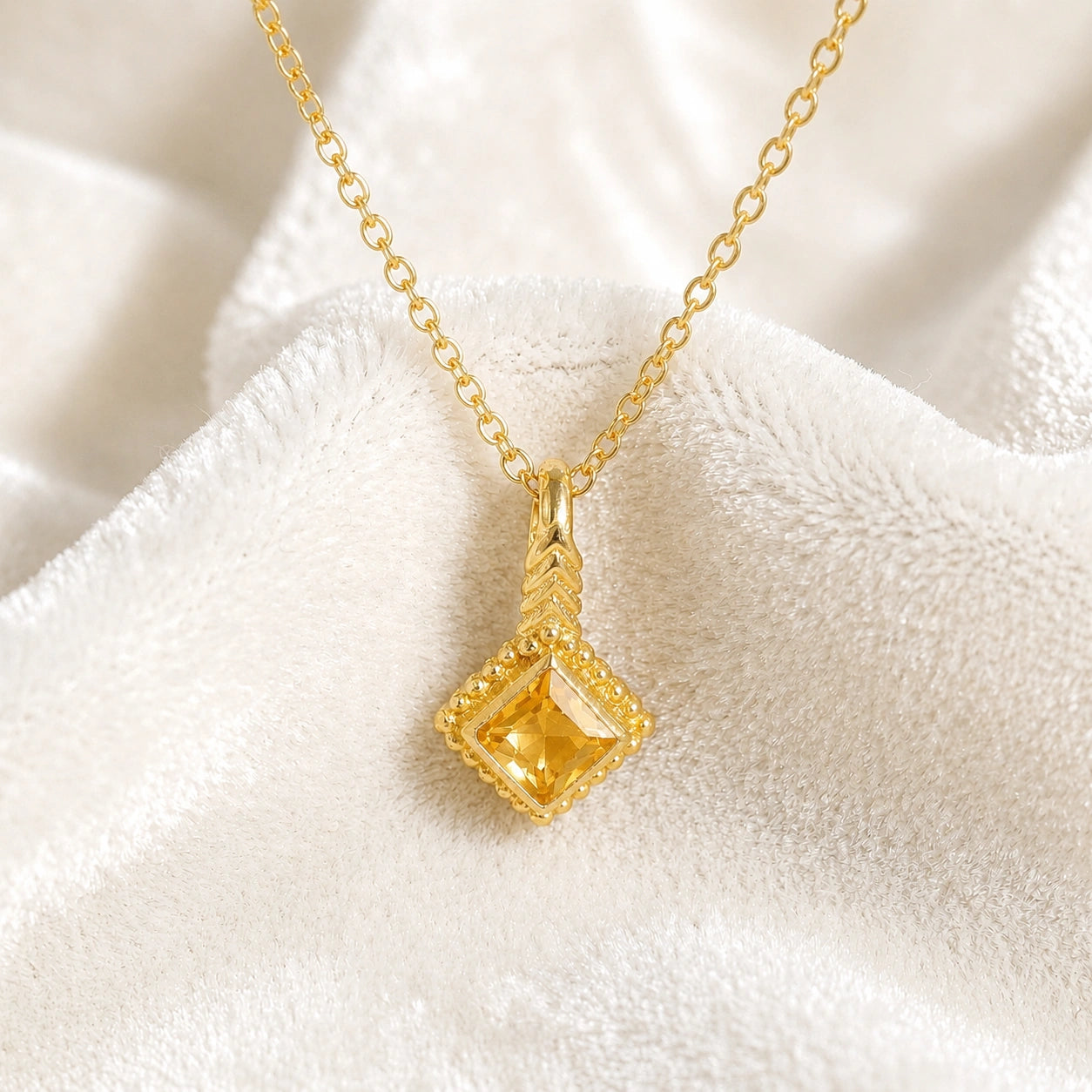 Birthstone_necklace_in_gold-plated_silver_with_square_cut_citrine_pendant_in_front_angle_view_on_soft_white_fabric_background