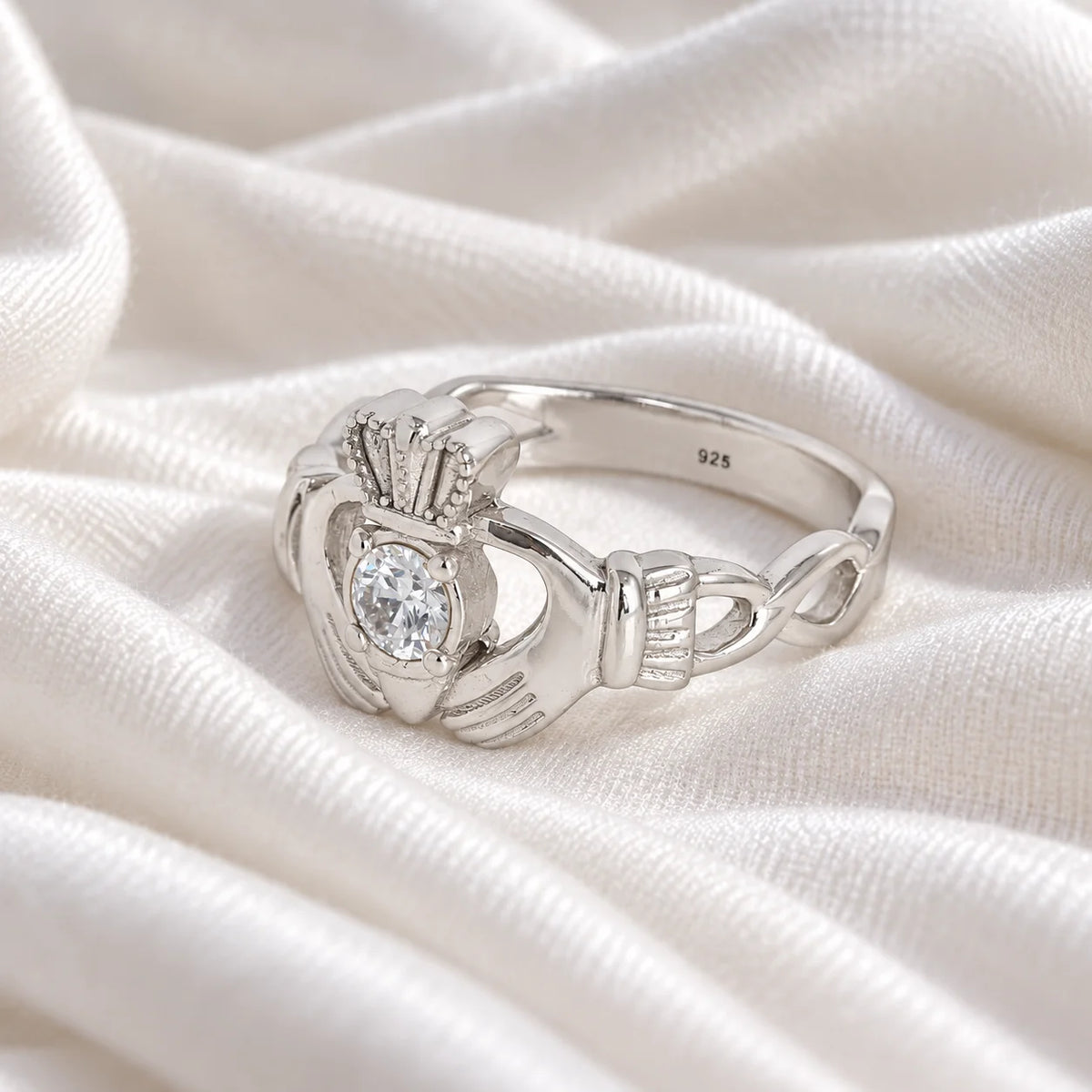 Claddagh_ring_in_sterling_silver_with_a_round_lab_grown_diamond_stone_at_slight_angle_view_on_soft_fabric_background