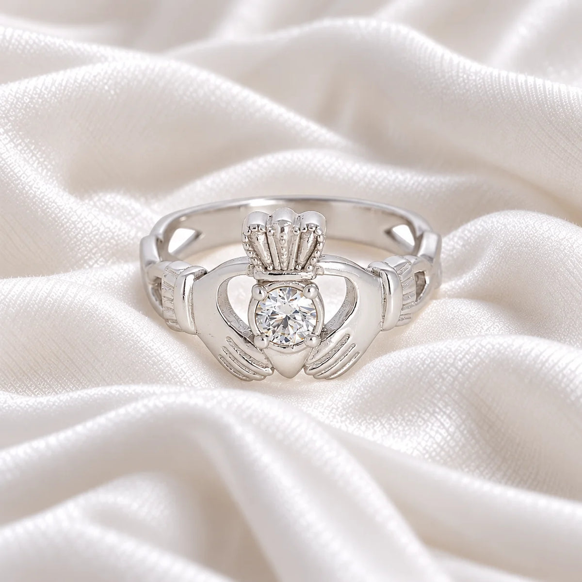Claddagh_ring_in_sterling_silver_with_a_round_CZ_stone_at_front_angle_view_on_soft_fabric_background