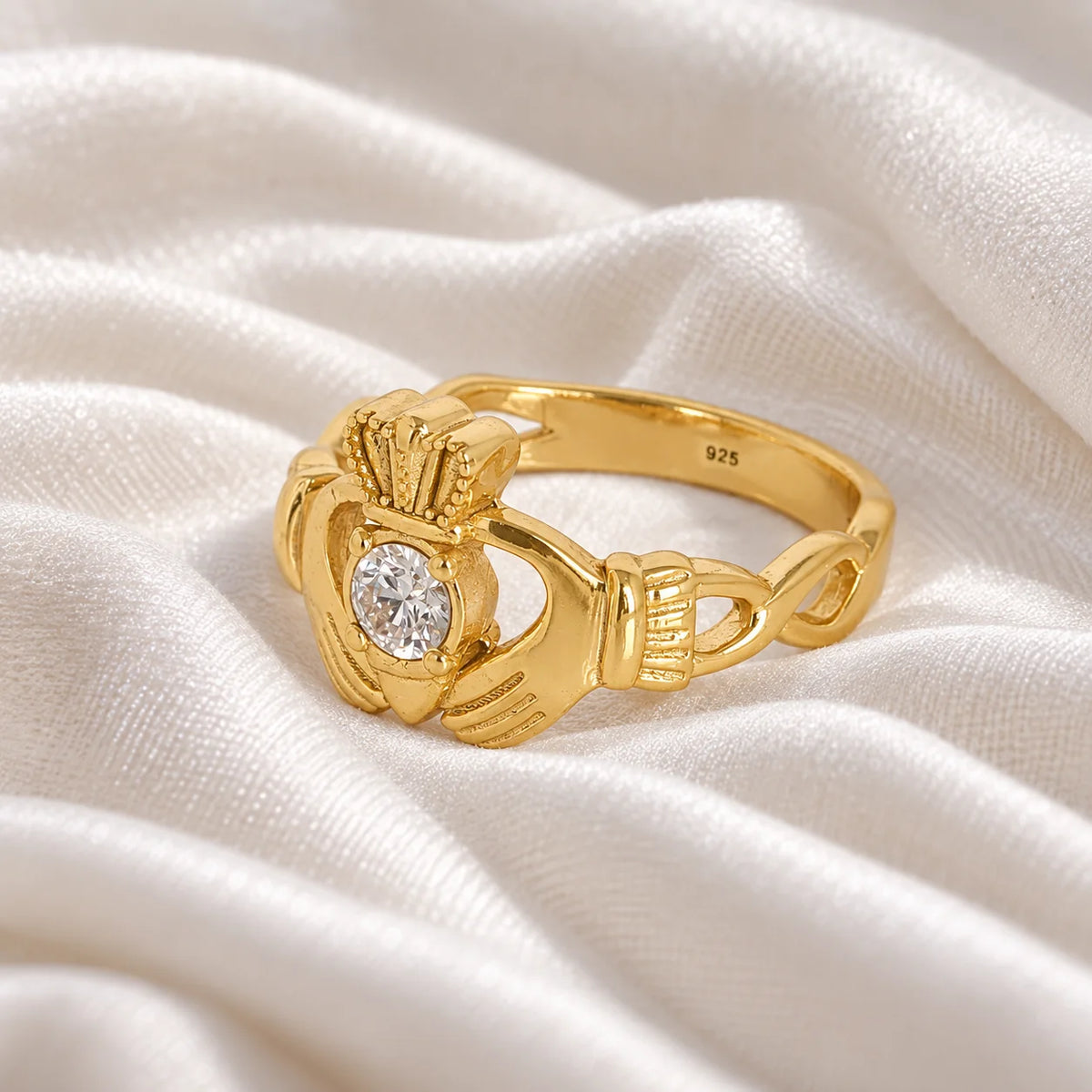 Claddagh_ring_in_gold_plated_silver_with_a_round_lab_grown_diamond_stone_at_slight_angle_view_on_soft_fabric_background