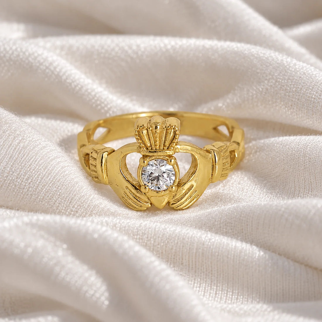 Claddagh_ring_in_gold_plated_silver_with_a_round_lab_grown_diamond_stone_at_front_angle_view_on_soft_fabric_background