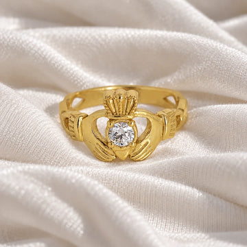 Claddagh_ring_in_gold_plated_silver_with_a_round_lab_grown_diamond_stone_at_front_angle_view_on_soft_fabric_background