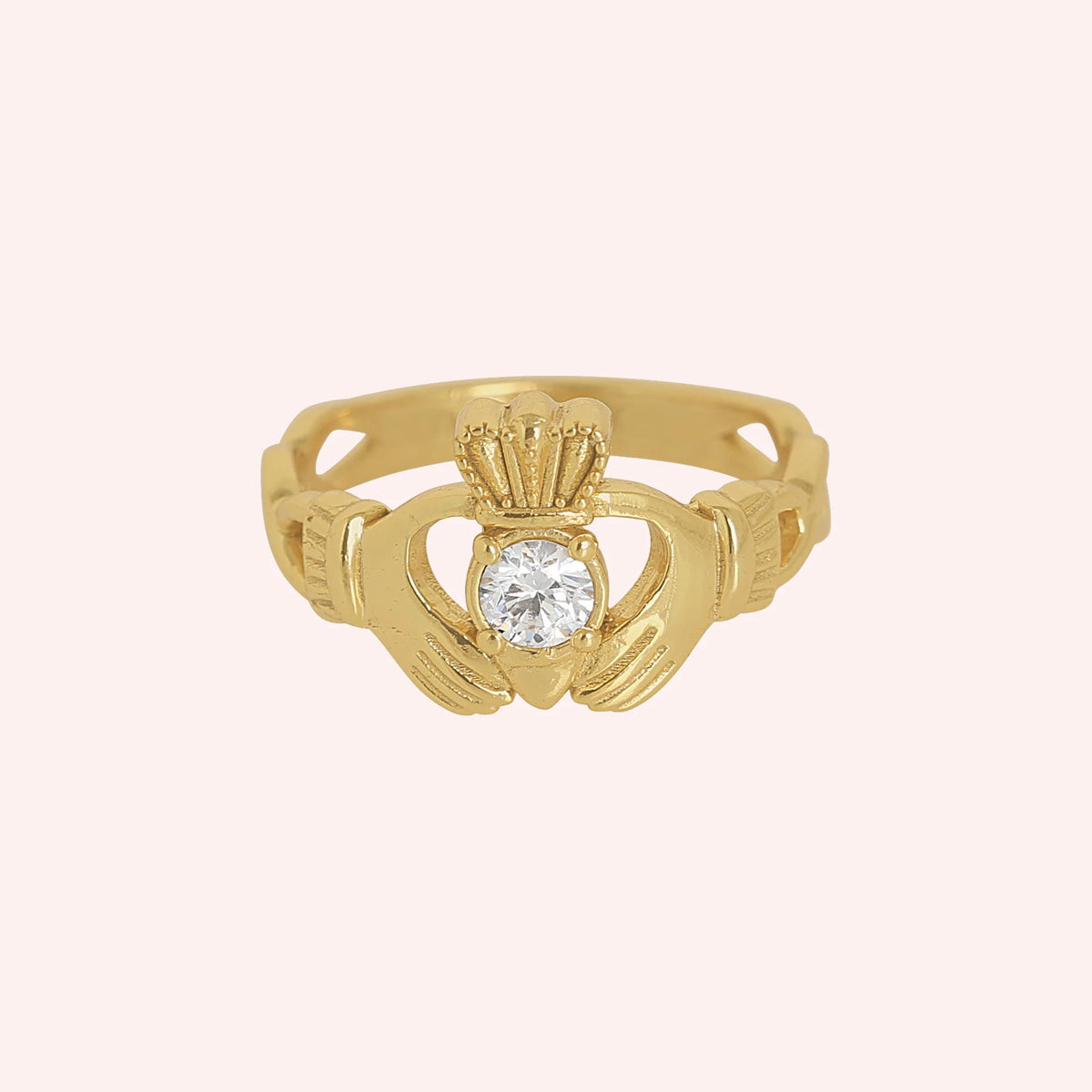 Claddagh_ring_in_gold_plated_silver_with_a_round_CZ_stone_at_front_angle_view_on_solid_pink_background