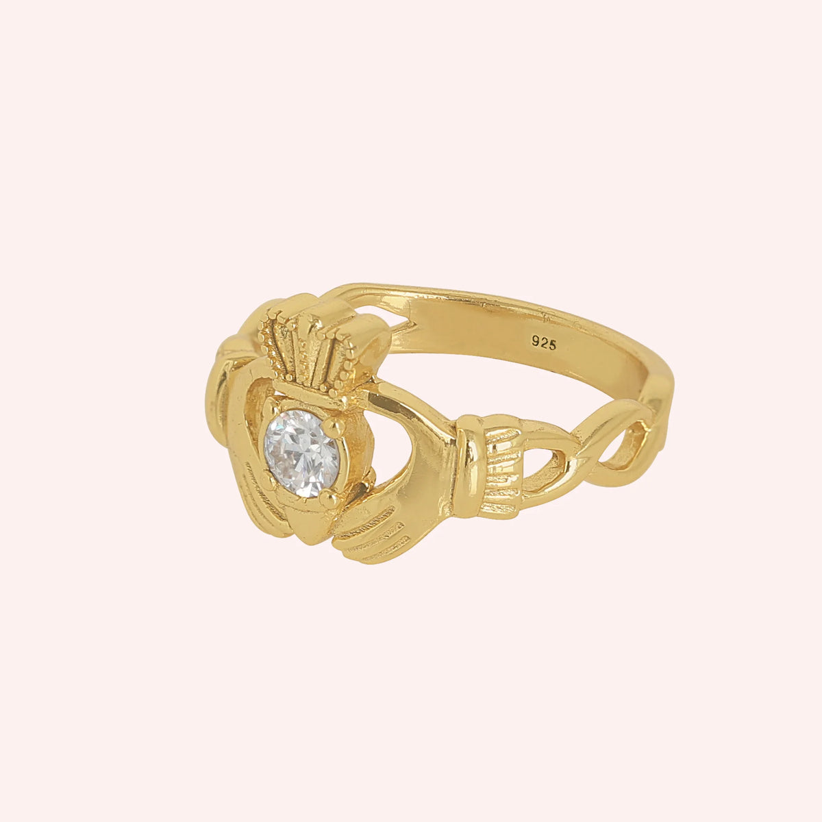 Claddagh_ring_in_gold_plated_silver_with_a_round_CZ_stone_at_side_angle_view_on_solid_pink_background