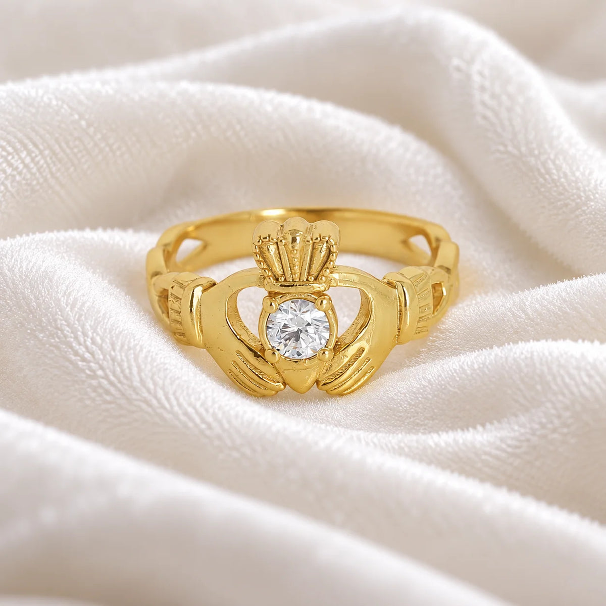 Claddagh_ring_in_gold_plated_silver_with_a_round_CZ_stone_at_front_angle_view_on_soft_fabric_background