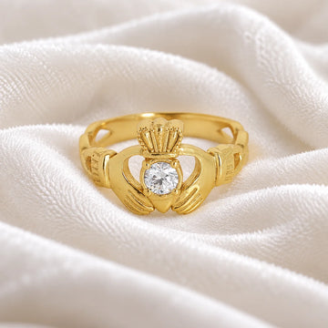 Claddagh_ring_in_gold_plated_silver_with_a_round_CZ_stone_at_front_angle_view_on_soft_fabric_background