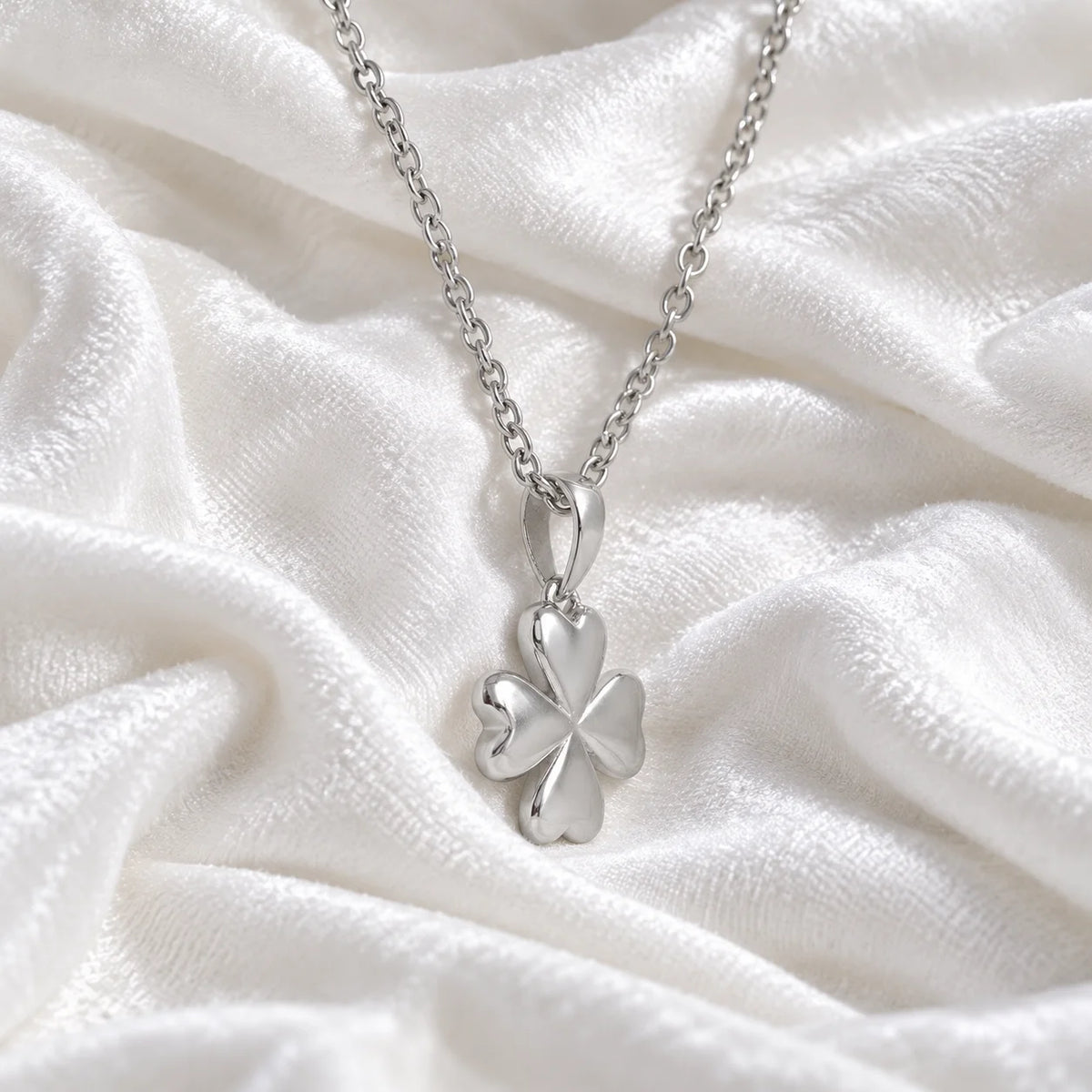 Clover_necklace_in_sterling_silver_with_four_leaves_design_at_slight_angle_view_on_soft_fabric_background