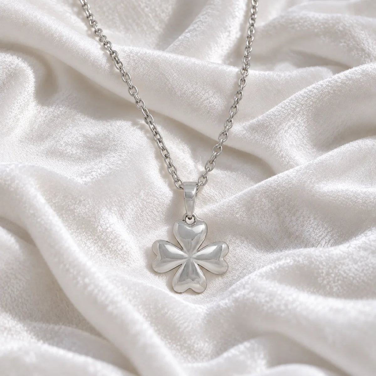 Clover_necklace_in_sterling_silver_with_four_leaves_design_at_front_angle_view_on_soft_fabric_background