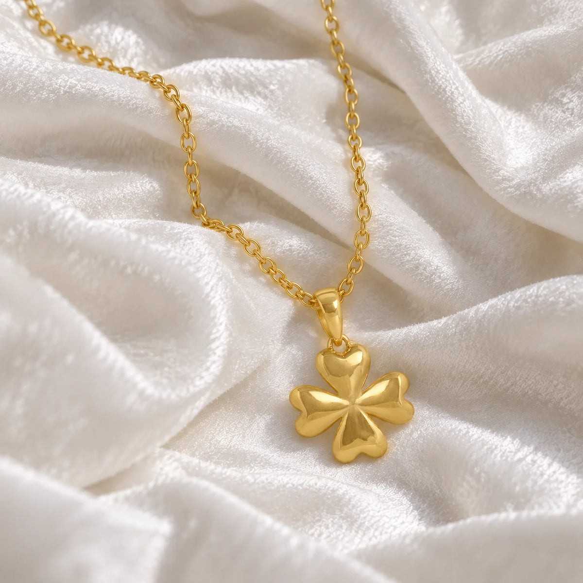 Clover_necklace_in_gold_plated_silver_with_four_leaves_design_at_front_angle_view_on_soft_fabric_background