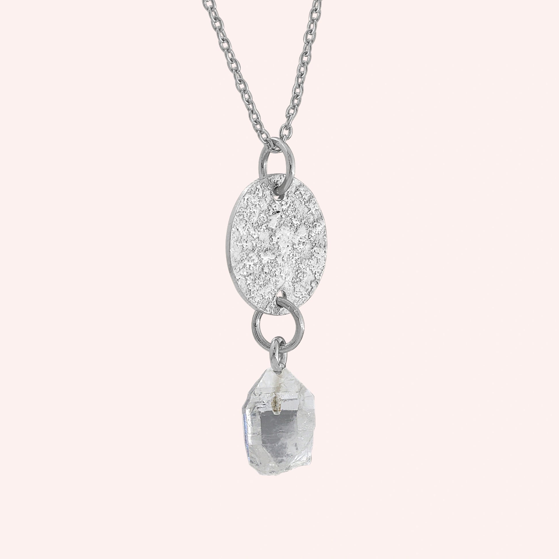 Coin_necklace_in_slight_angled_view_with_textured_round_pendant_sterling_silver_and_herkimer_stone_on_solid_pink_background