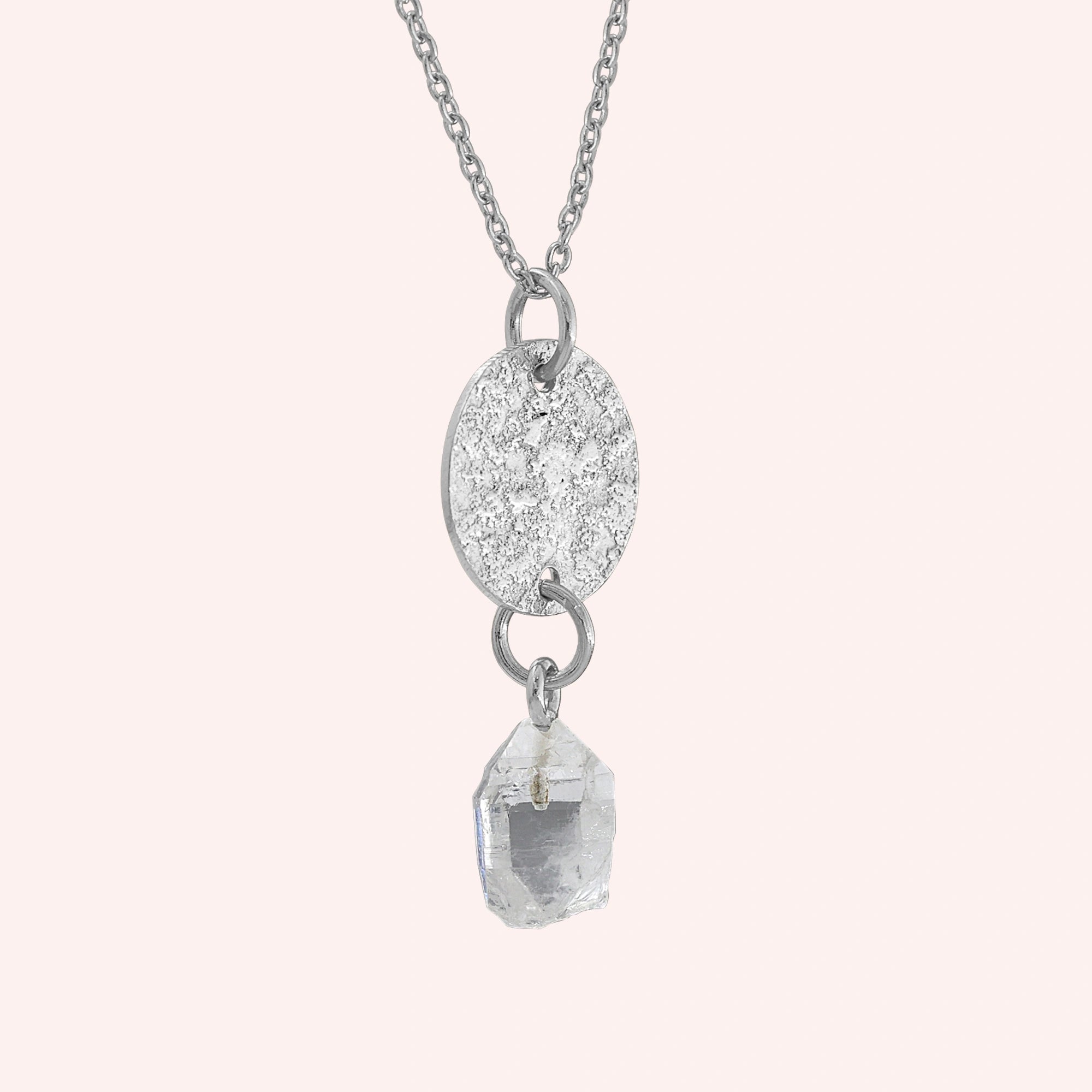 Coin_necklace_in_slight_angled_view_with_textured_round_pendant_sterling_silver_and_herkimer_stone_on_solid_pink_background