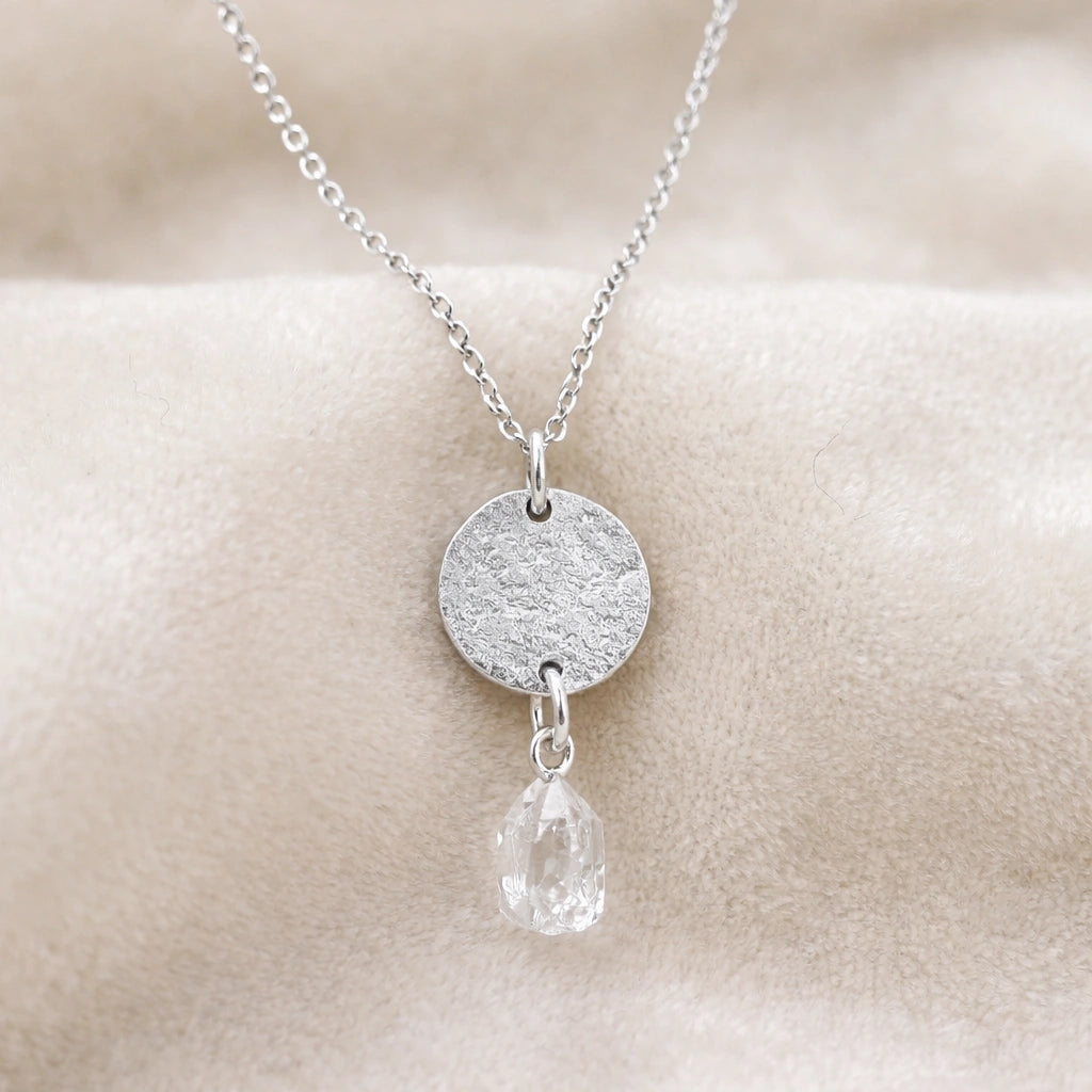 Coin_necklace_in_front_angled_view_with_textured_round_pendant_sterling_silver_and_herkimer_stone_on_soft_fabric_background