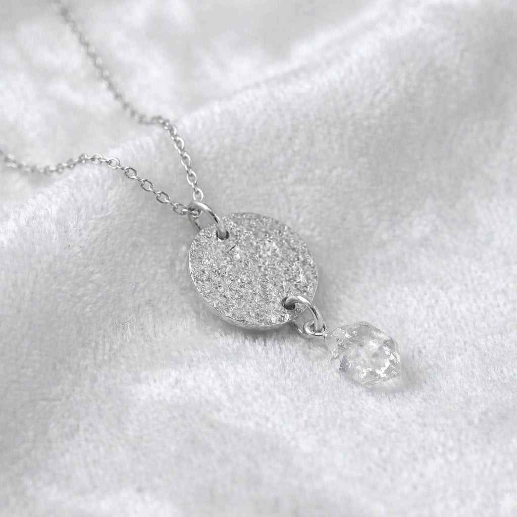 Coin_necklace_in_slight_angled_view_with_textured_round_pendant_sterling_silver_and_herkimer_stone_on_soft_fabric_background