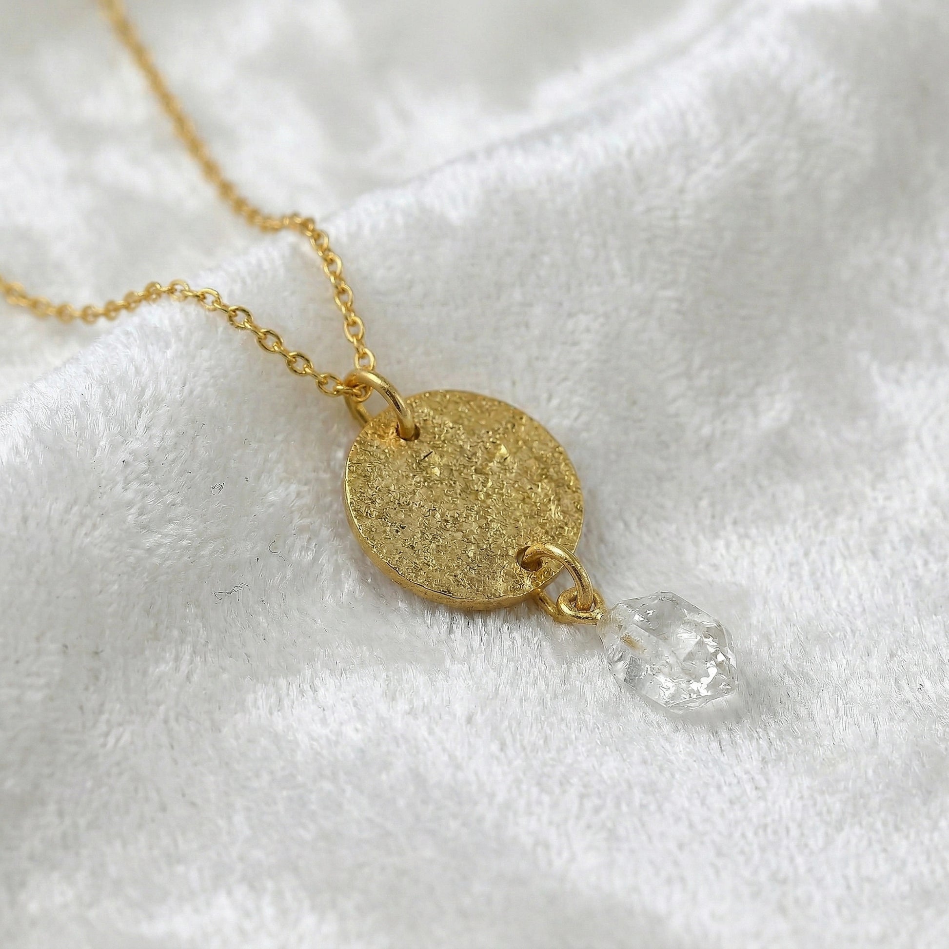 Coin_necklace_in_slight_angled_view_with_textured_round_pendant_gold_plated_silver_and_herkimer_stone_on_soft_fabric_background