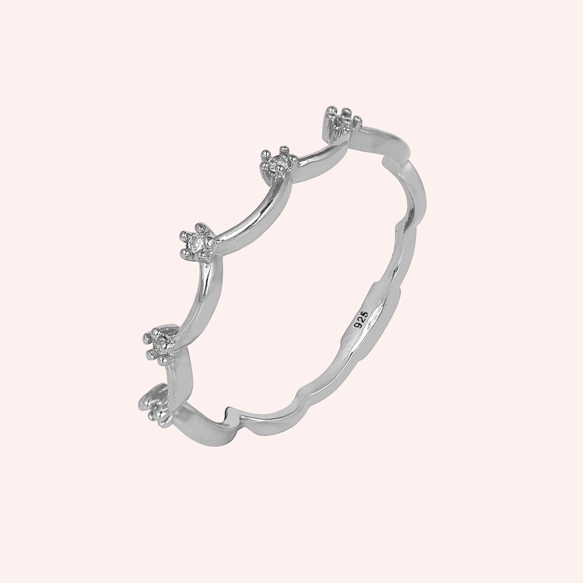 A sterling silver crown ring featuring white topaz stones and a tiara ring design at a side angle on a light pink background