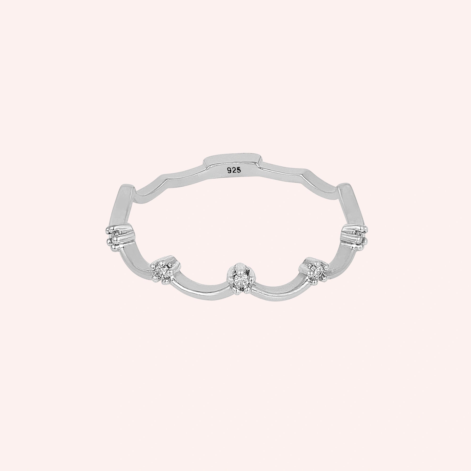 A sterling silver crown ring with small white topaz and a tiara ring design at a front angle over a pale pink plain background