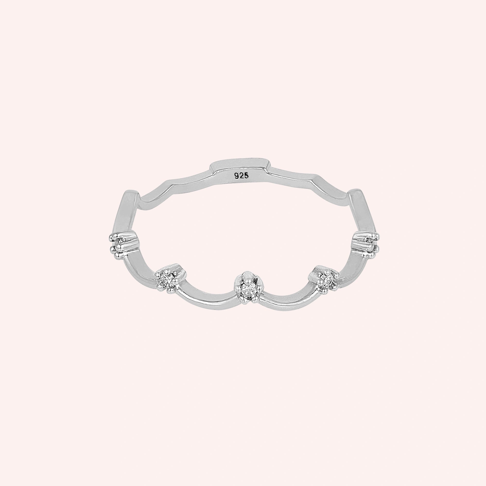 A sterling silver crown ring with small white topaz and a tiara ring design at a front angle over a pale pink plain background