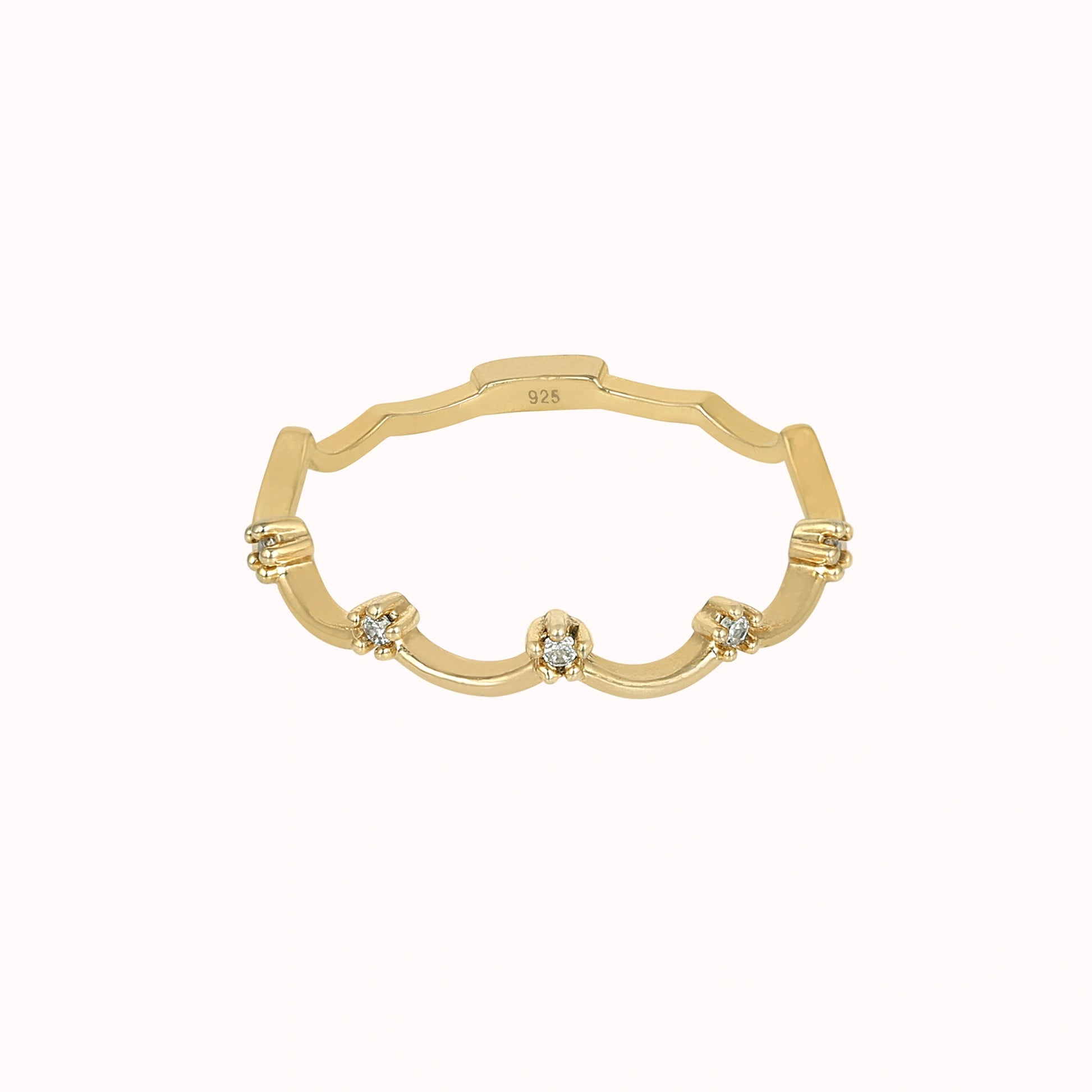 A gold plated crown ring with a scalloped tiara ring design with white topaz at a front angle on a pale pink background