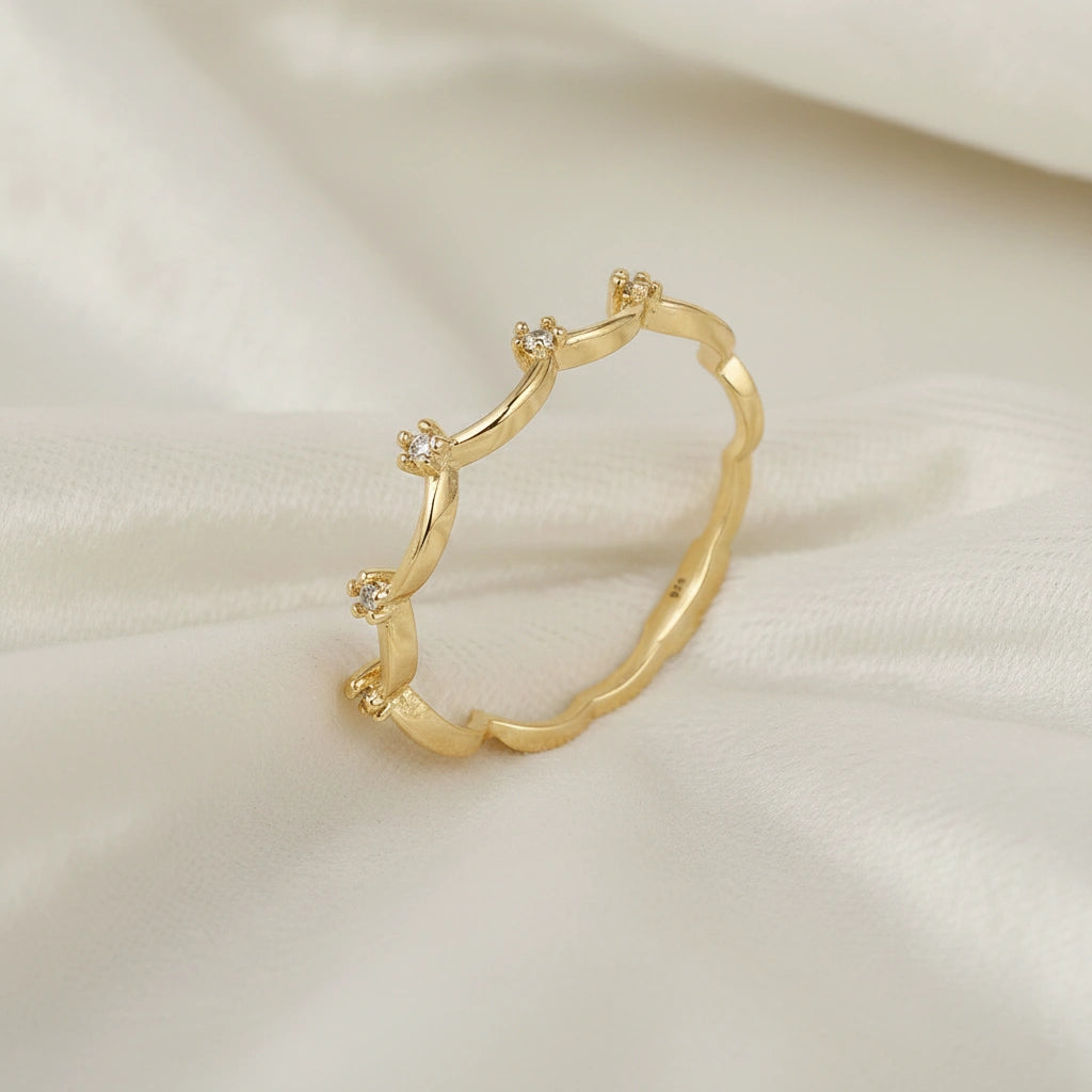 A gold plated crown ring with white topaz and a tiara ring design at a side angle over an off white fabric background
