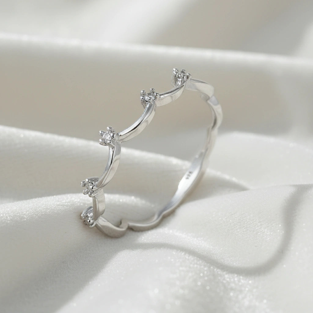 A sterling silver crown ring featuring white topaz stones and a tiara ring design at a side angle on a white fabric background