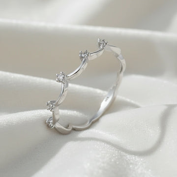 A sterling silver crown ring featuring white topaz stones and a tiara ring design at a side angle on a white fabric background
