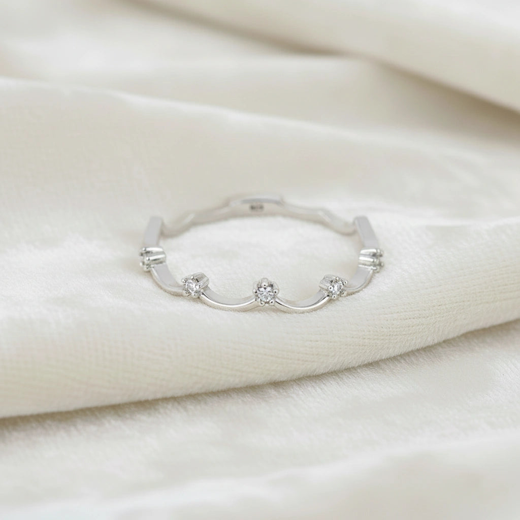 A sterling silver crown ring with small white topaz and a tiara ring design at a front angle over a white fabric background