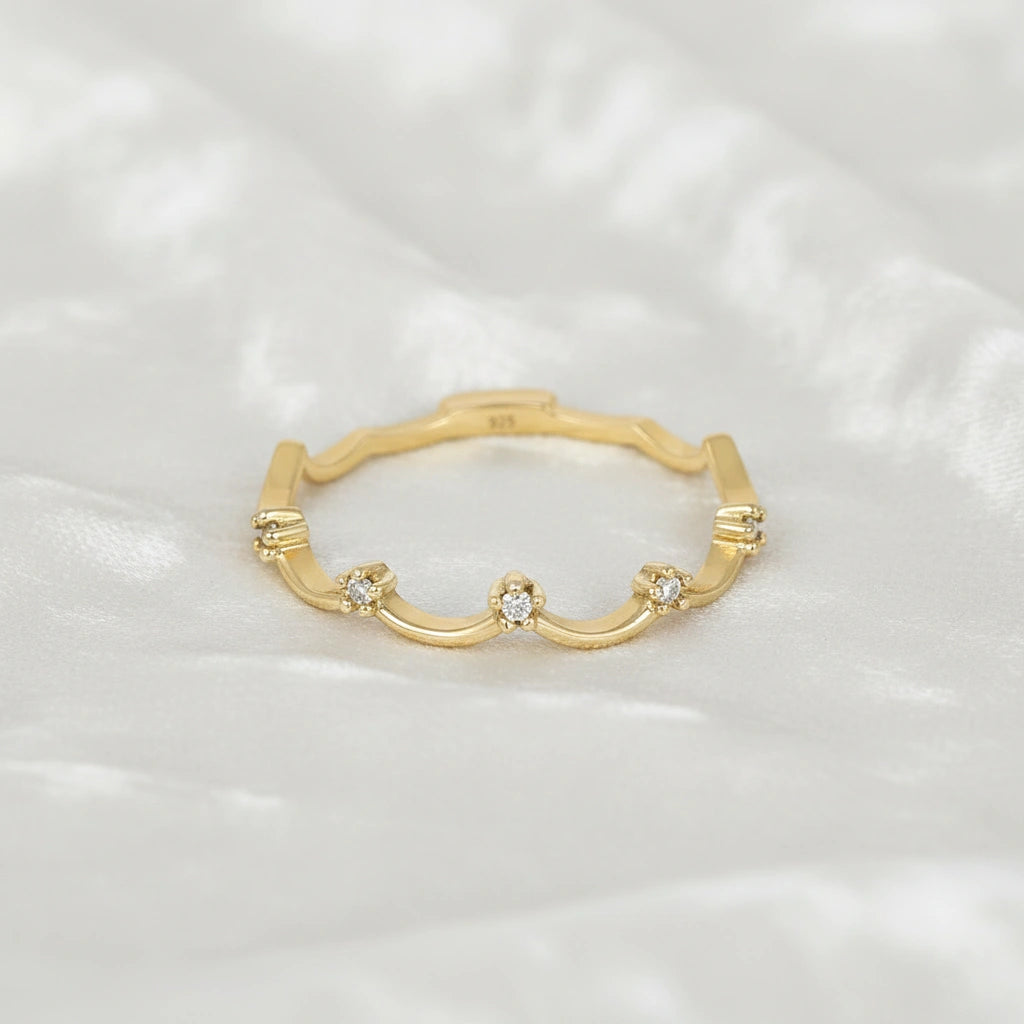 A gold plated crown ring with a scalloped tiara ring design with white topaz at a front angle on a white fabric background
