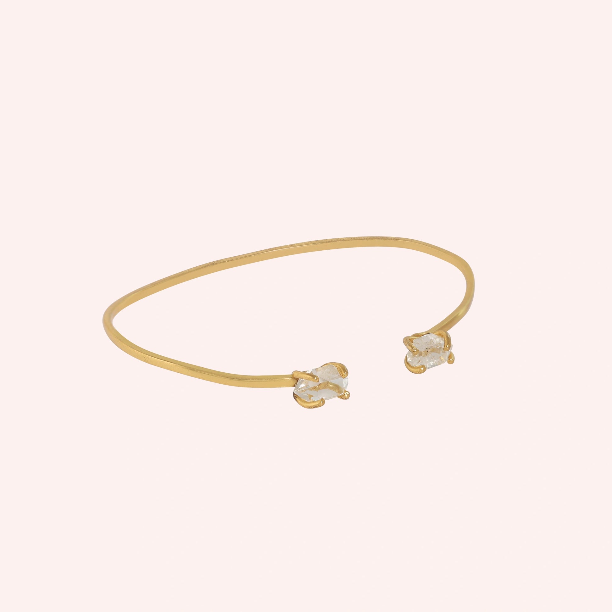Crystal_bracelet_in_gold_plated_silver_with_two_raw_herkimer_stones_at_slight_angle_view_on_solid_pink_background