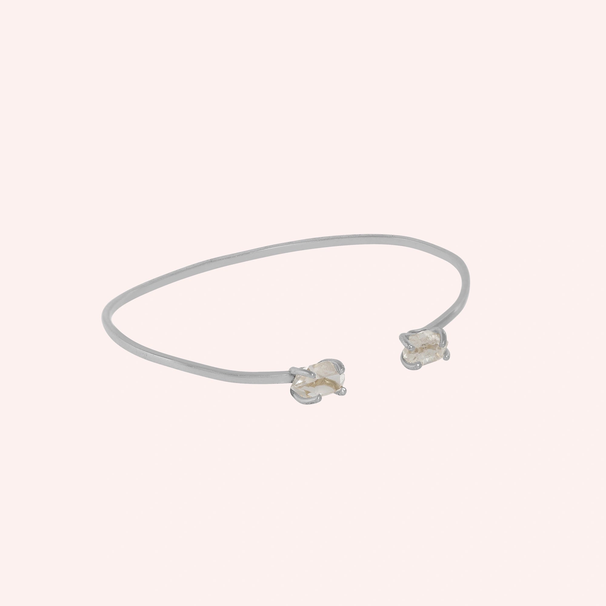 Crystal_bracelet_in_sterling_silver_with_two_raw_herkimer_stones_at_slight_angle_view_on_solid_pink_background