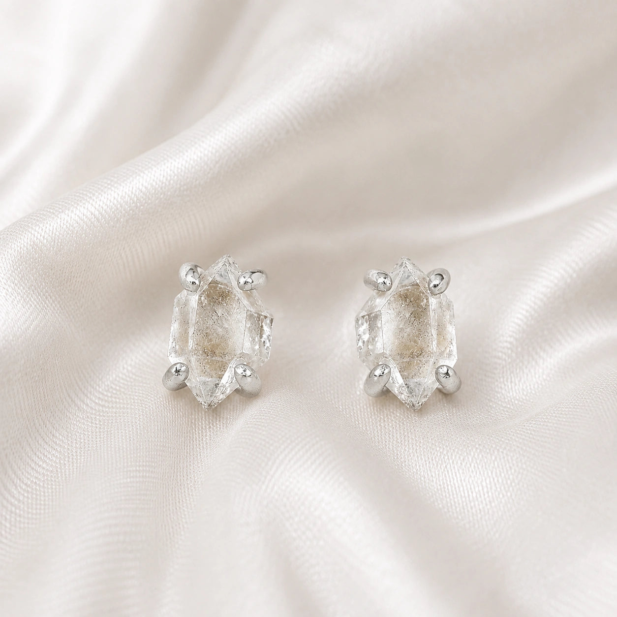 Crystal_earrings_in_sterling_silver_with_raw_herkimer_stone_at_front_angle_view_on_soft_fabric_background