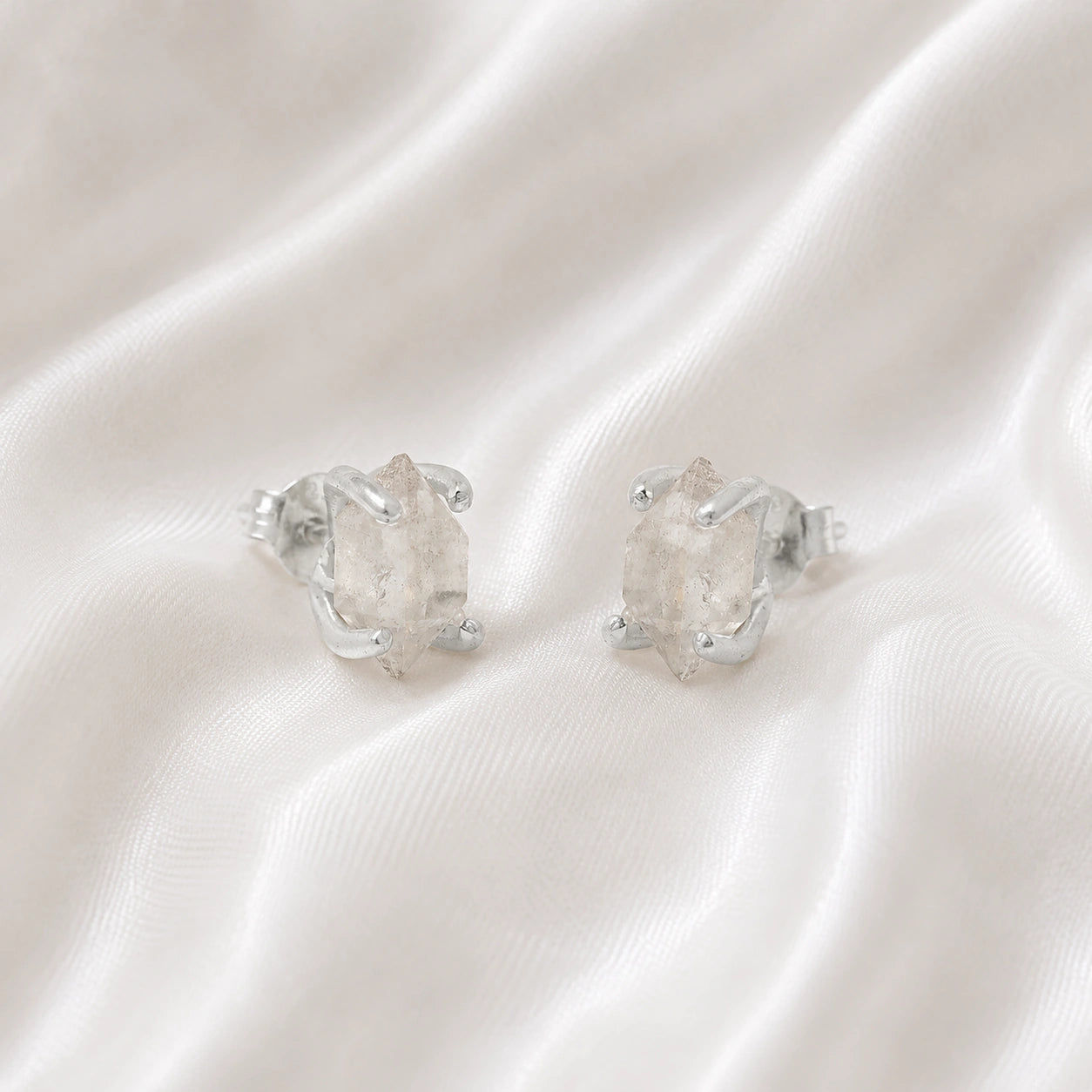 Crystal_earrings_in_sterling_silver_with_raw_herkimer_stone_at_slight_angle_view_on_soft_fabric_background