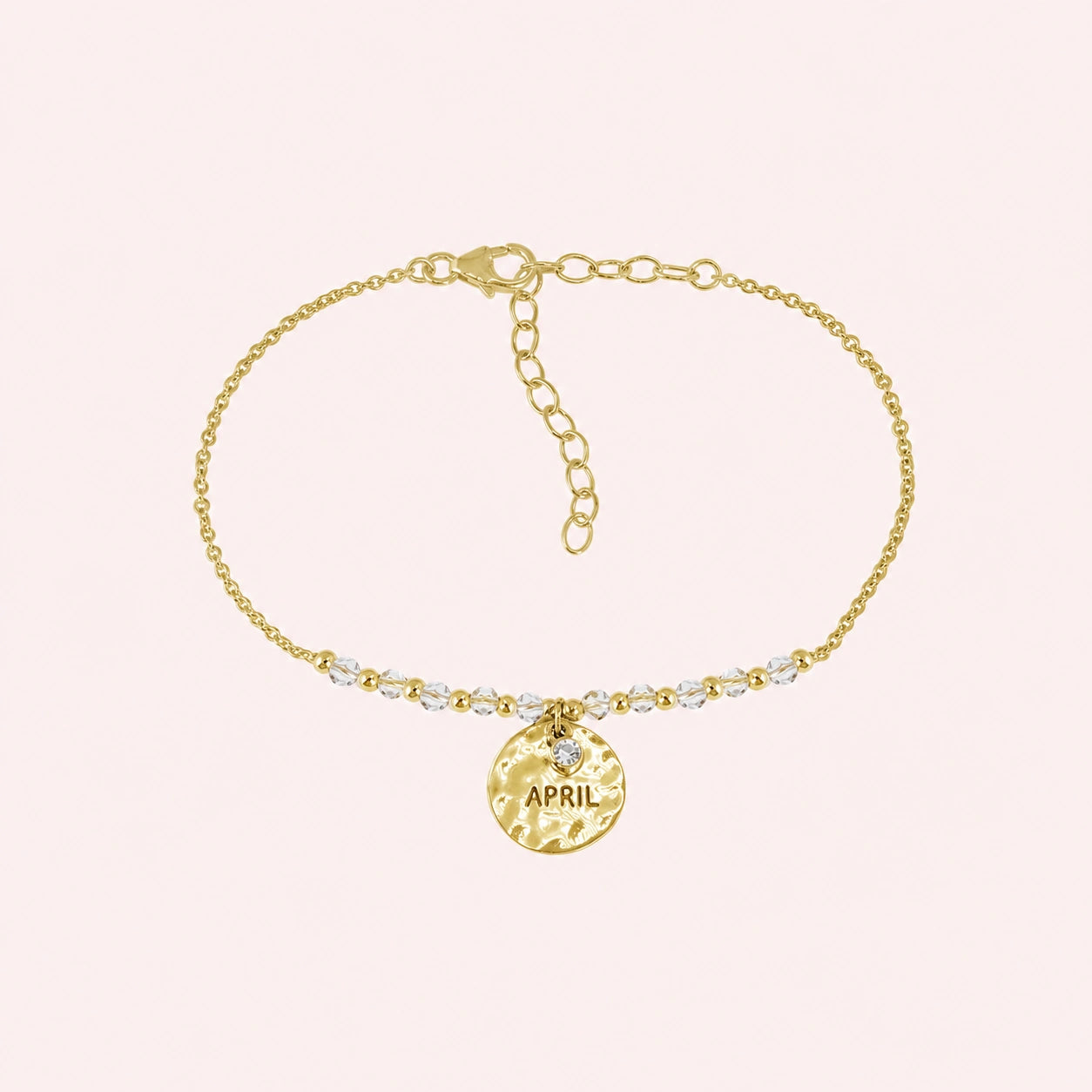 Birthstone_bracelet_in_gold_plated_silver_with_April_charm_and_crystal_beads_on_fine_chain_on_solid_pink_background
