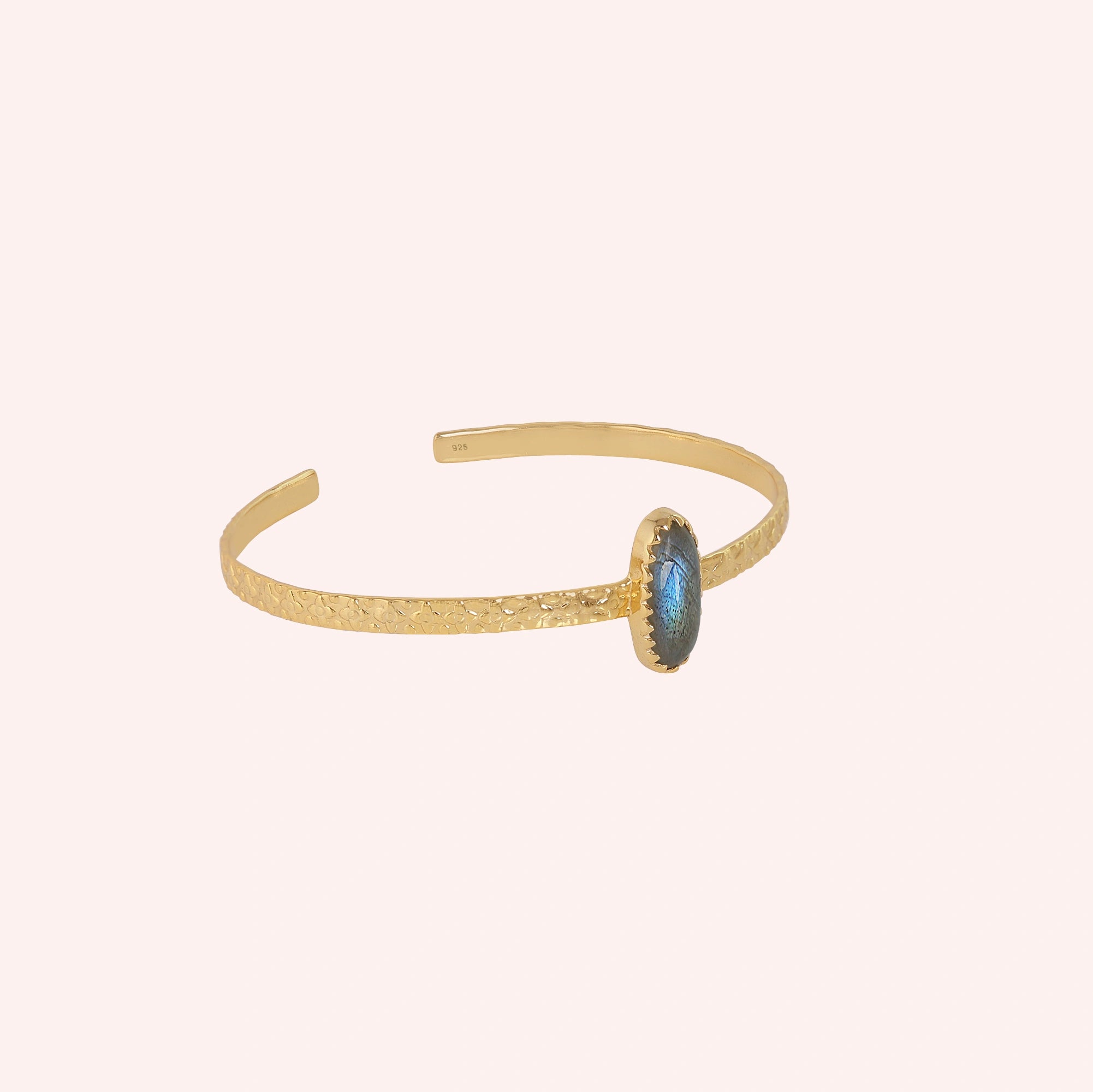 Cuff_bracelet_in_gold_plated_silver_with_an_oval_labradorite_stone_at_slight_angle_view_on_solid_pink_background