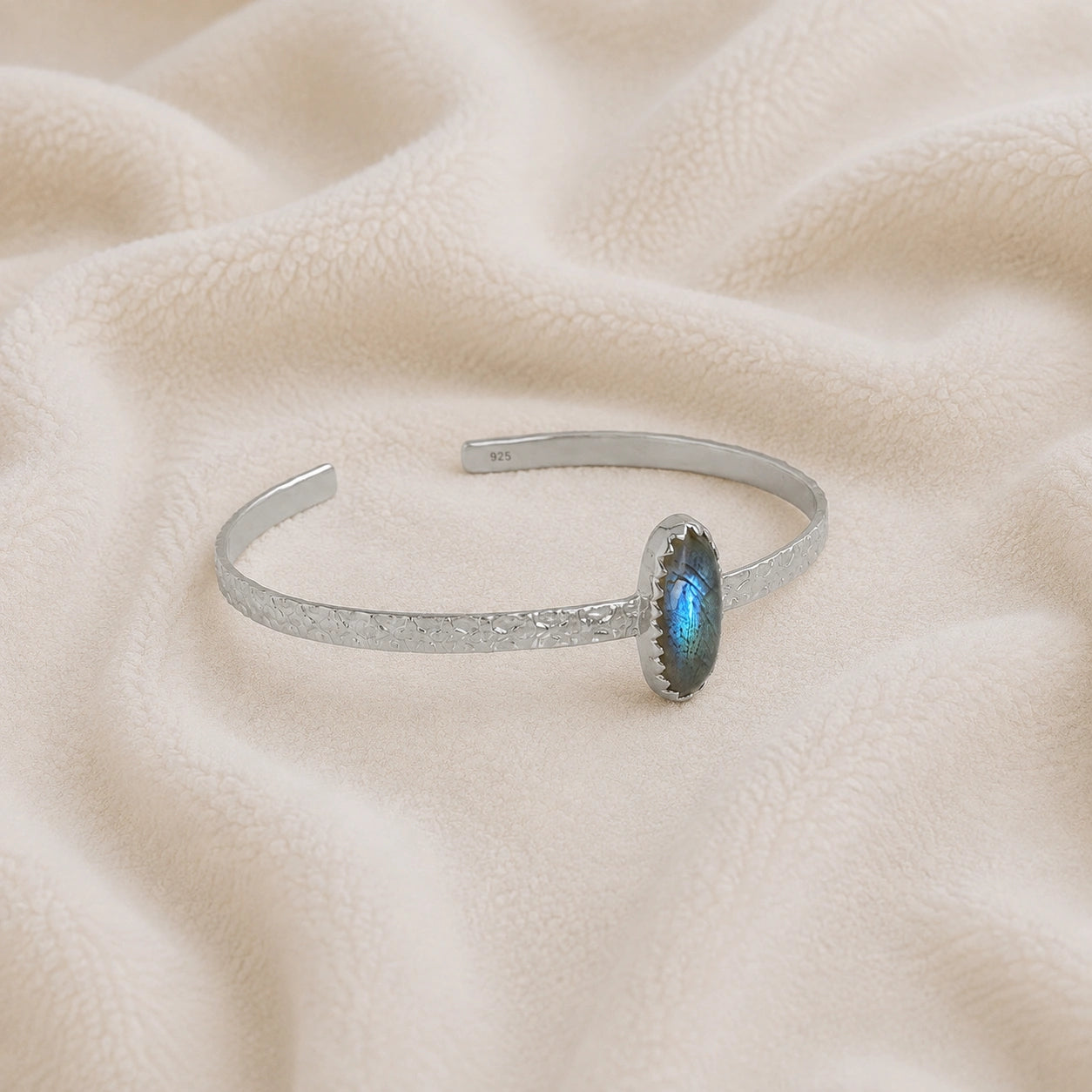 Cuff_bracelet_in_sterling_silver_with_an_oval_labradorite_stone_at_slight_angle_view_on_soft_fabric_background