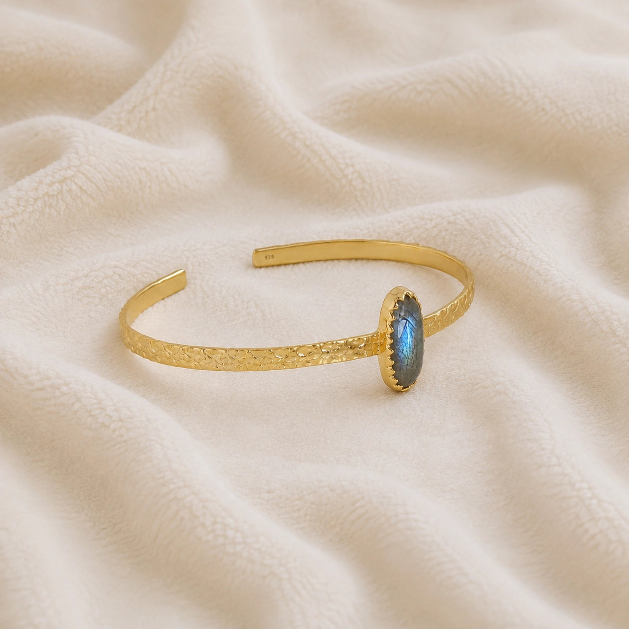 Cuff_bracelet_in_gold_plated_silver_with_an_oval_labradorite_stone_at_slight_angle_view_on_soft_fabric_background