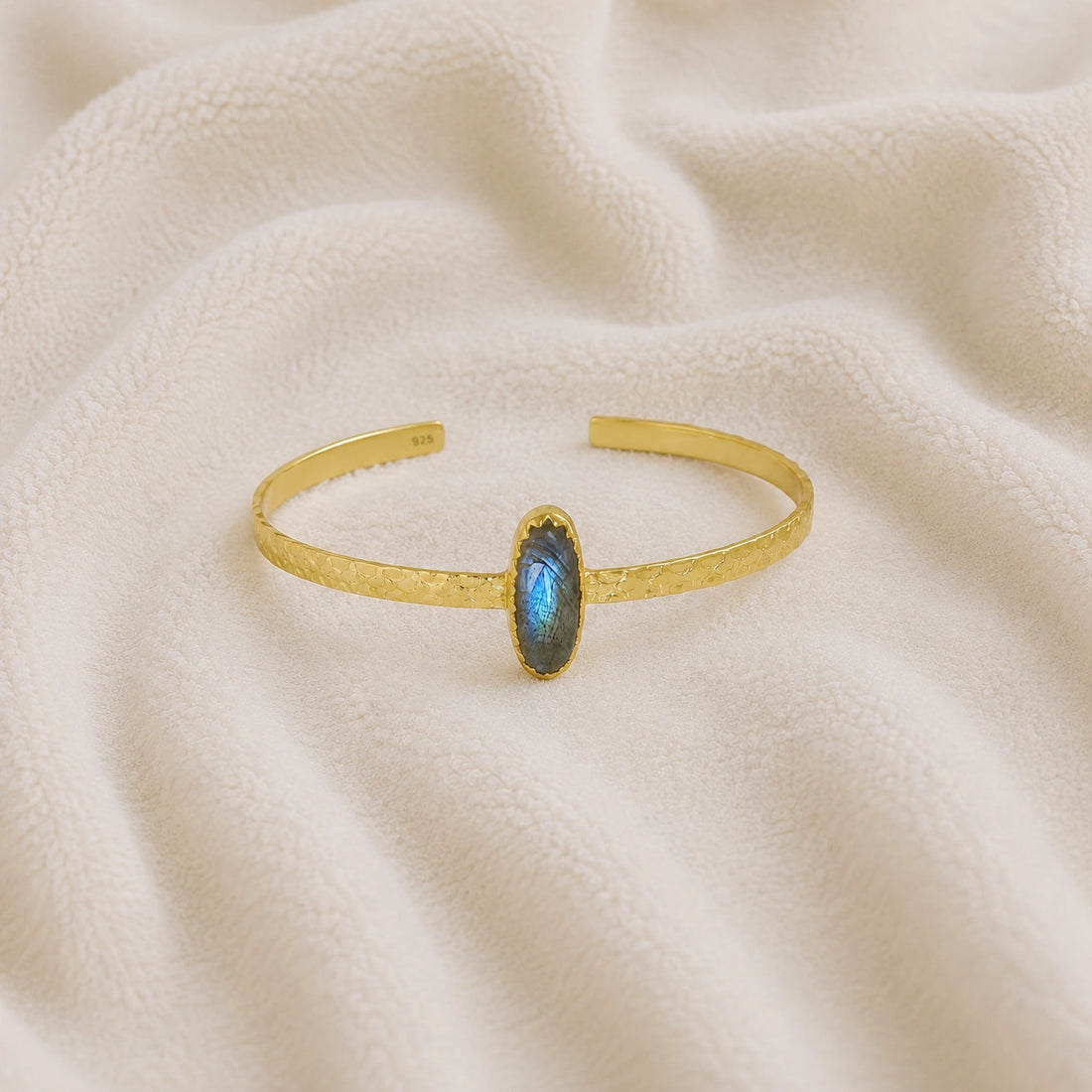 Cuff_bracelet_in_gold_plated_silver_with_an_oval_labradorite_stone_at_front_angle_view_on_soft_fabric_background