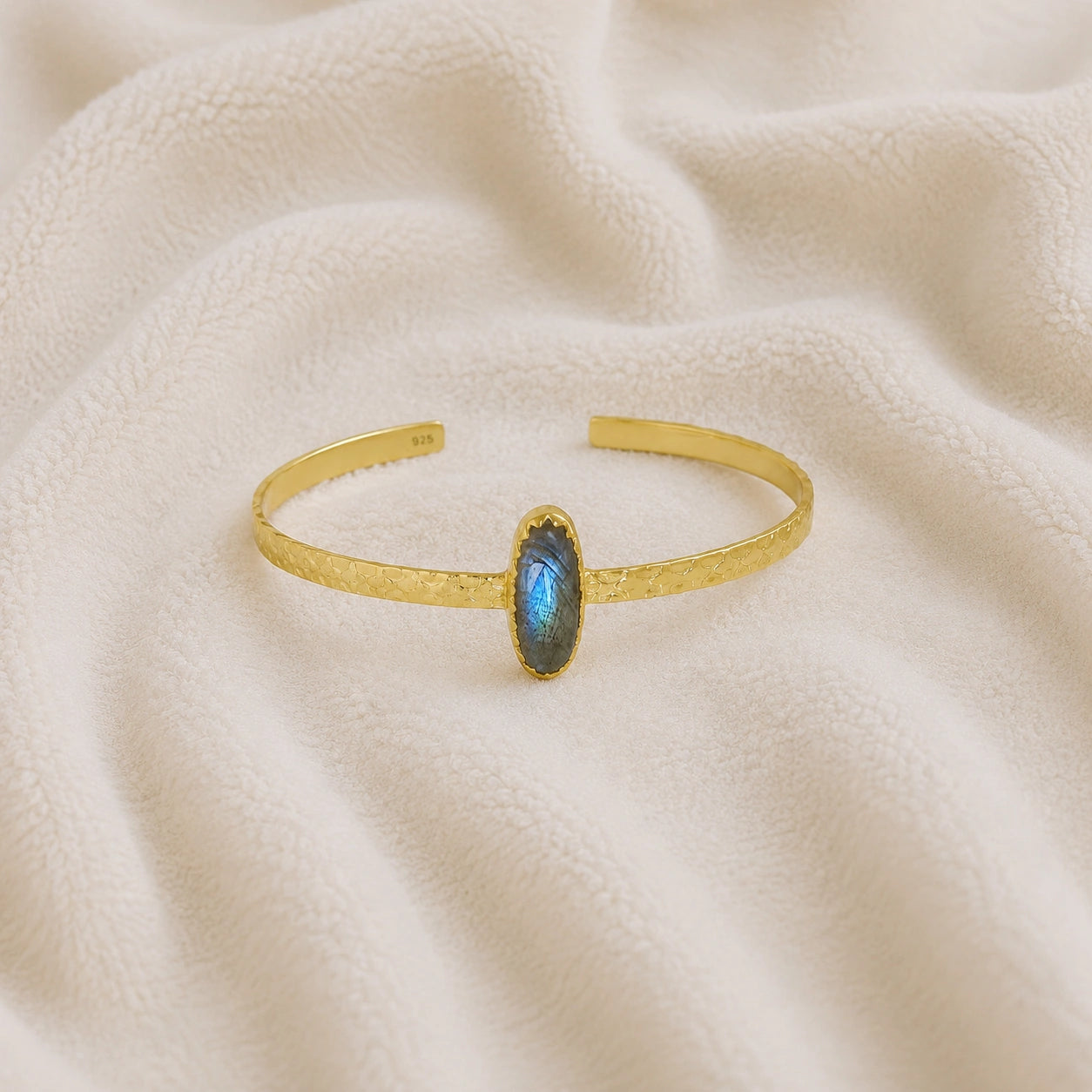 Cuff_bracelet_in_gold_plated_silver_with_an_oval_labradorite_stone_at_front_angle_view_on_soft_fabric_background