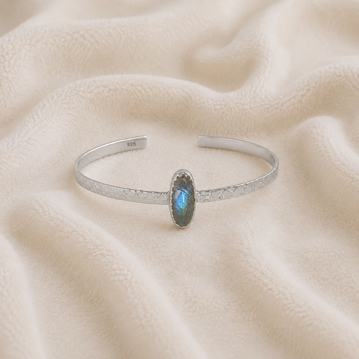 Cuff_bracelet_in_sterling_silver_with_an_oval_labradorite_stone_at_front_angle_view_on_soft_fabric_background