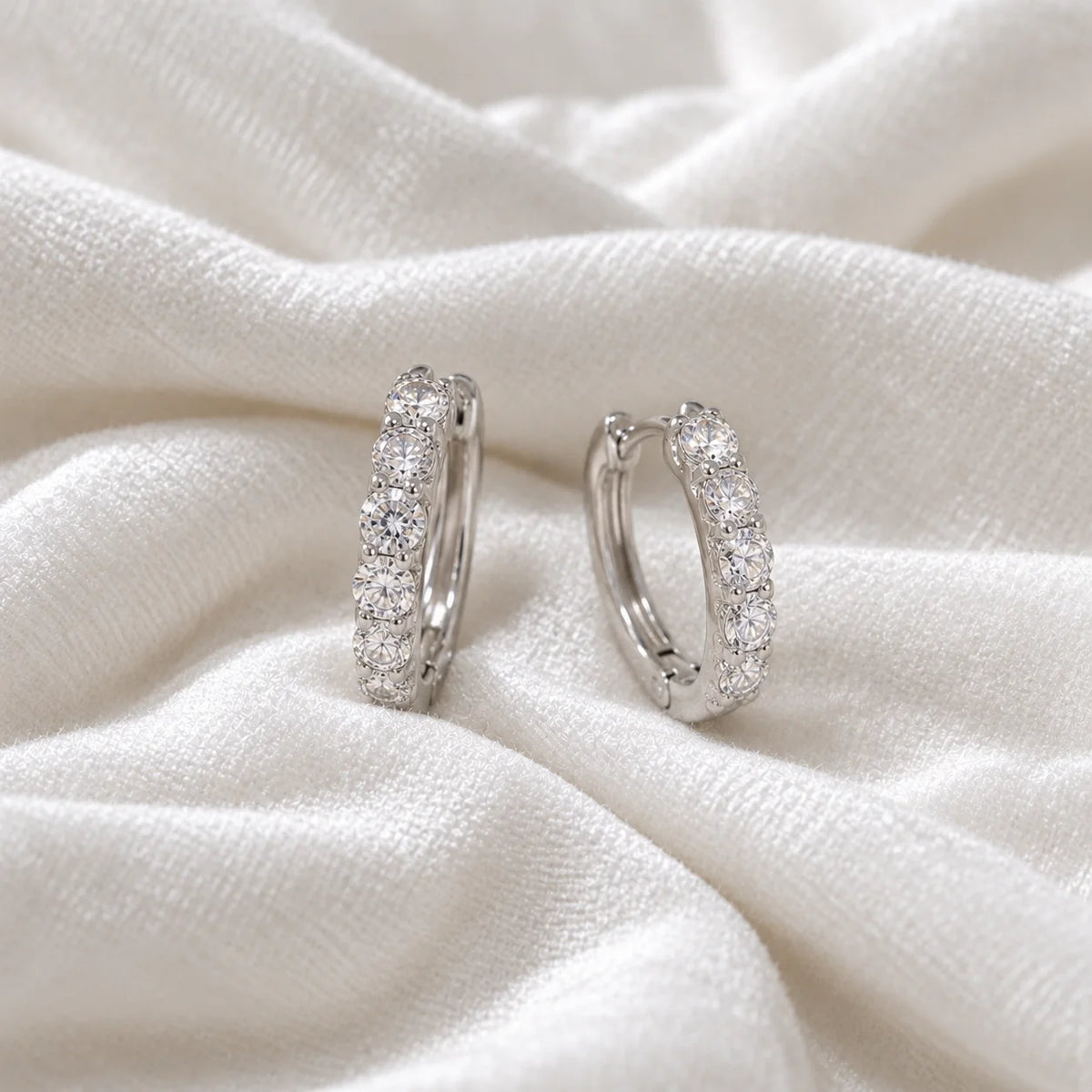 Cute_earrings_in_sterling_silver_with_CZ_stones_at_side_angle_view_on_soft_fabric_background