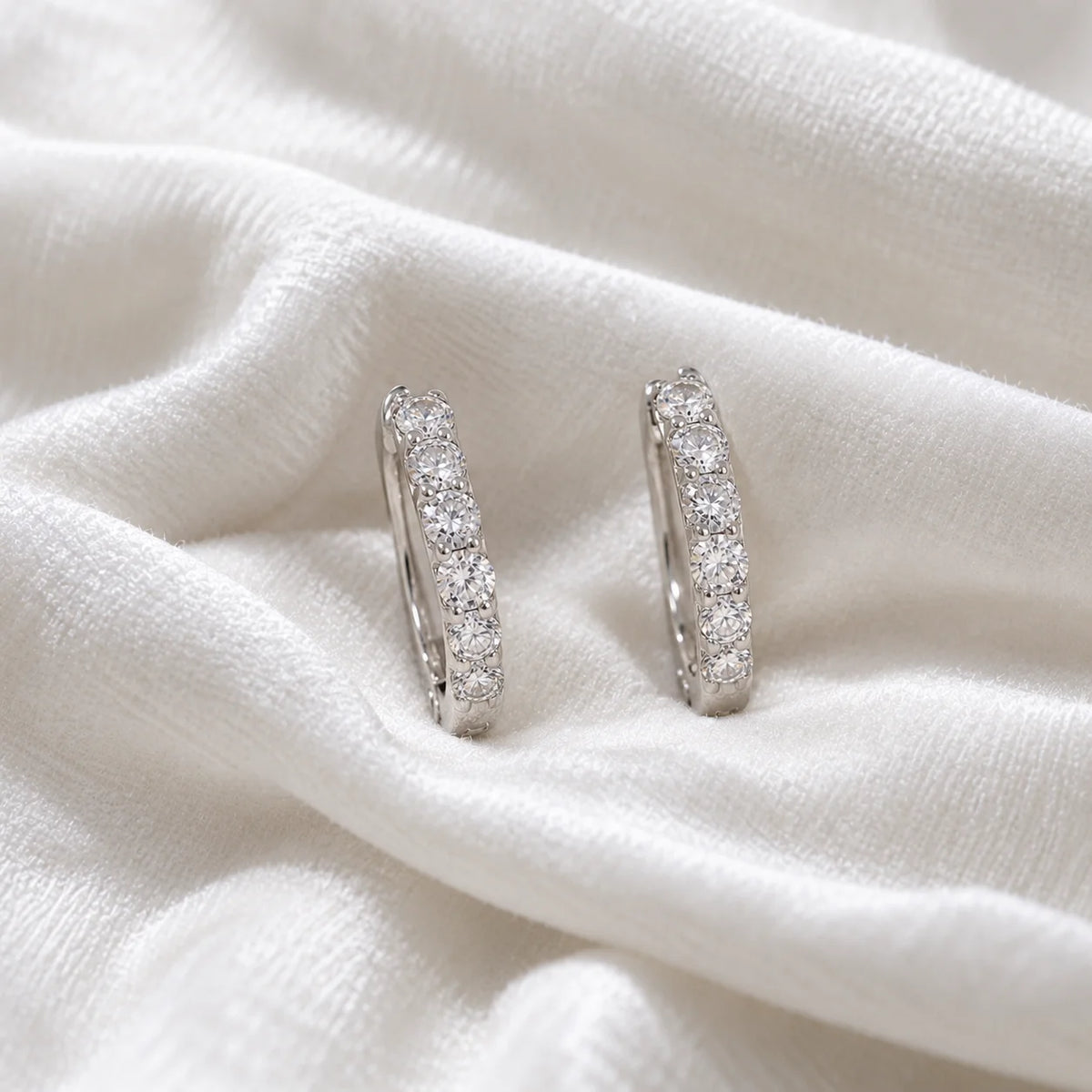 Cute_earrings_in_sterling_silver_with_CZ_stones_at_front_angle_view_on_soft_fabric_background