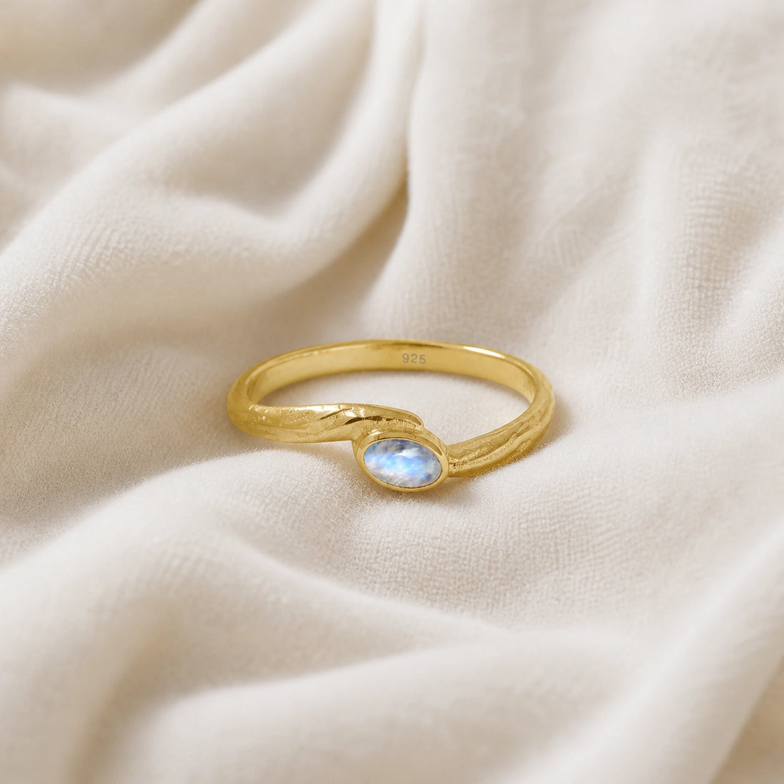 Cute_ring_gold_plated_silver_with_oval_moonstone_and_textured_wave_band_shown_at_front_angle_on_soft_fabric_background